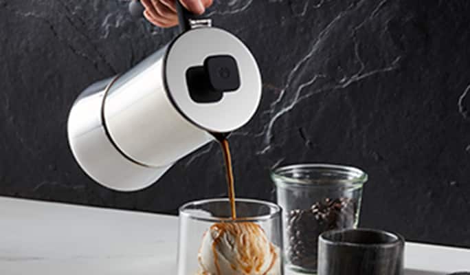 A hand pouring coffee from a stainless steel French press into a glass.
