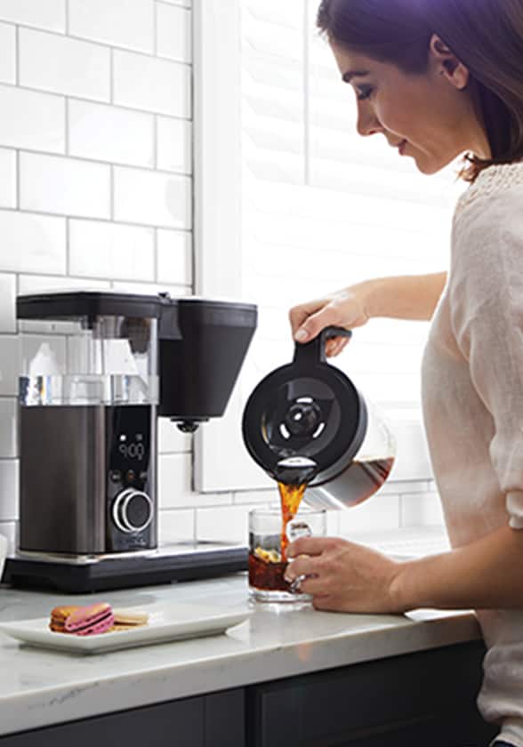 Une femme se versant une tasse de café devant une cafetière noire posée sur un comptoir.