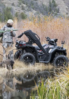 Un homme debout avec son équipement de chasse, derrière son VTT. 