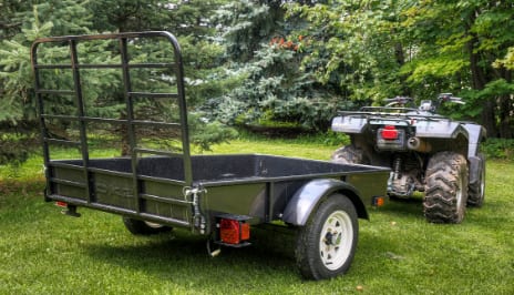 A trailer attached to an ATV, parked in a lush green patch. 