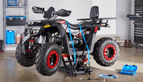 A black all-terrain vehicle sits strapped to the top of an ATV jack next to an open blue toolbox inside a garage.