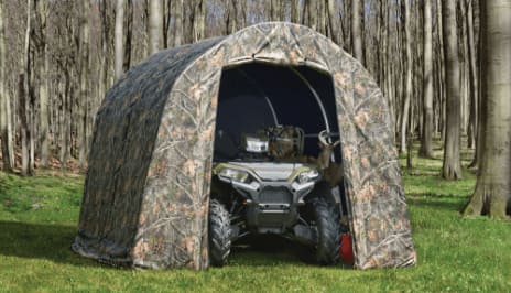 An all-terrain vehicle parked inside a camouflaged shelter set up in a forest clearing.