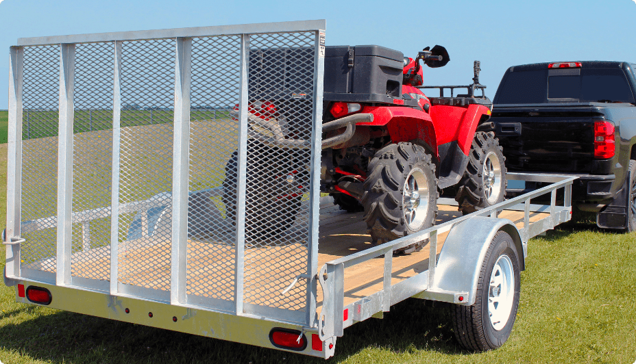 A red ATV rests in the bed of a True North Galvanized Utility Trailer hitched to a black pickup truck. 