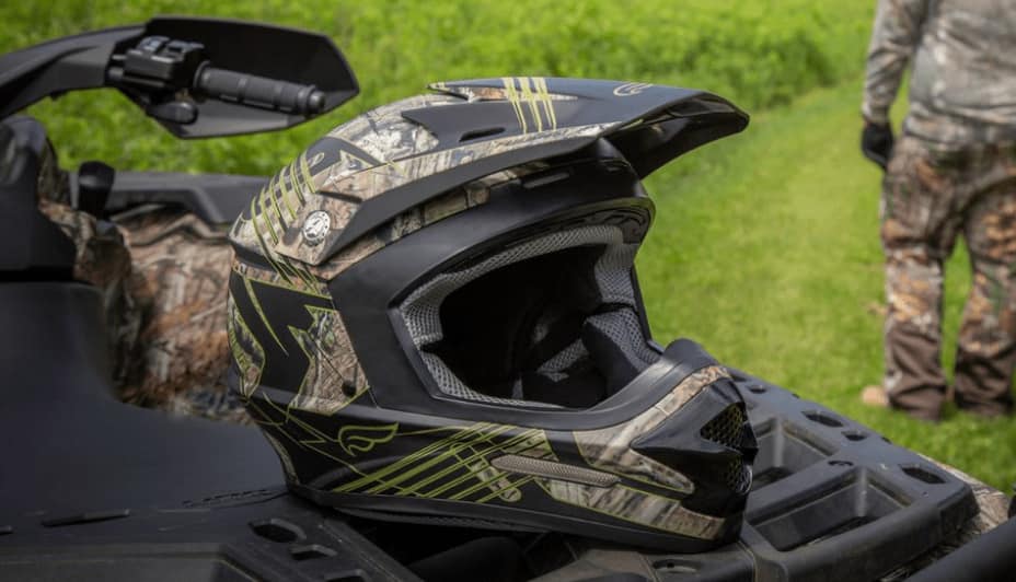 A black ATV helmet with a camouflage pattern rests on a black ATV. 