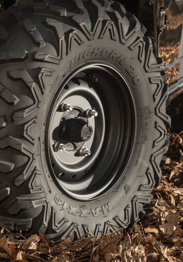A close-up of an Maxxis ATV tire resting on ground covered in dry leaves.