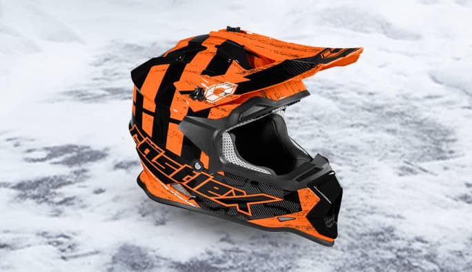 An orange-and-black snowmobile helmet rests on the ground in front of a grey garage door.
