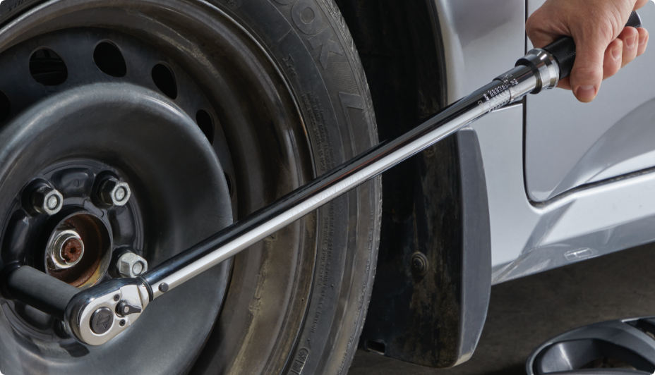 Une main appliquant une clé en croix argentée sur l'écrou de roue d'un pneu de voiture.