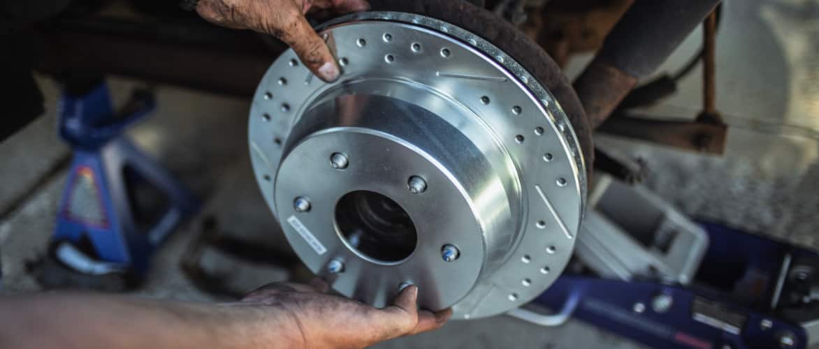 A pair of hands holds a silver brake rotor inside an auto garage.