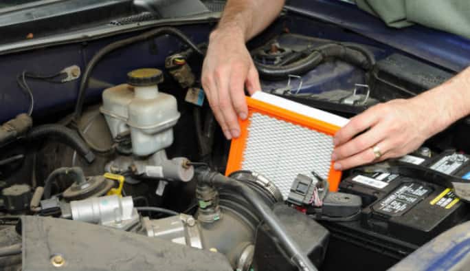 Hands insert a new air filter into a car’s engine.