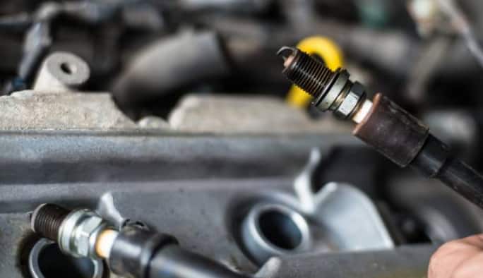 Close-up of hands replacing the spark plugs in a vehicle’s engine.