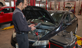 Man replacing battery under hood of car