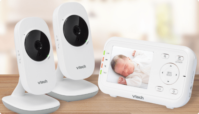 Two VTech cameras sit to the left of a VTech VM3252-2 Digital Video Baby Monitor with the image of a sleeping baby on its screen.