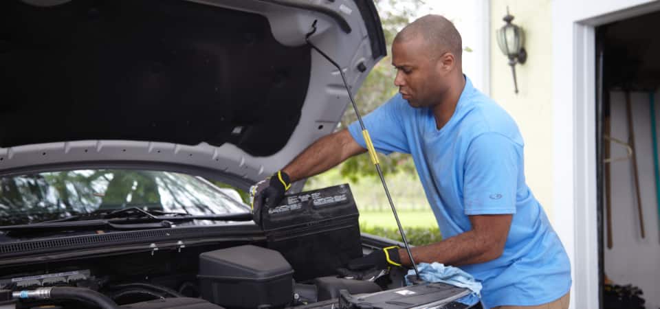 Man wearing gloves inspecting under front hood of car