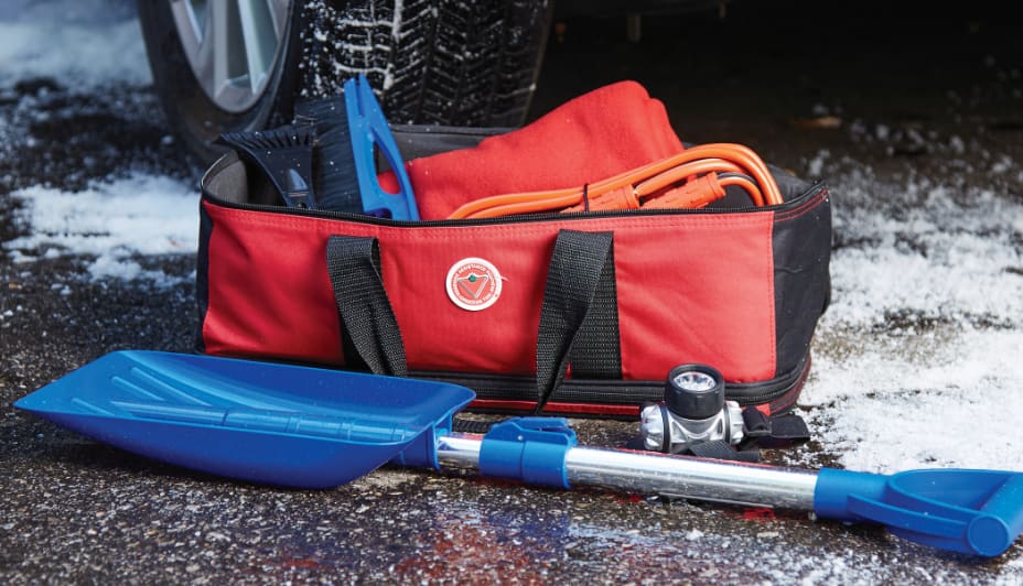 Red bag and blue shovel on ground next to car tire