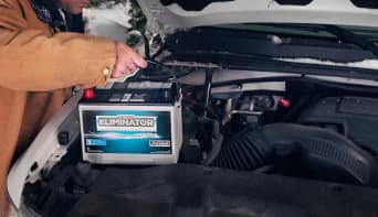 Man installing car battery under the front hood of car