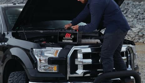 Man starting battery in front hood of truck