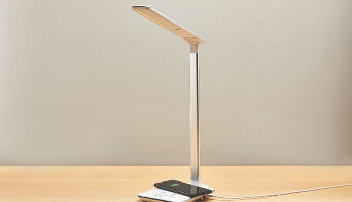 Un tapis de recharge sans fil Bluehive avec lampe à DEL est posé sur un bureau en bois. 