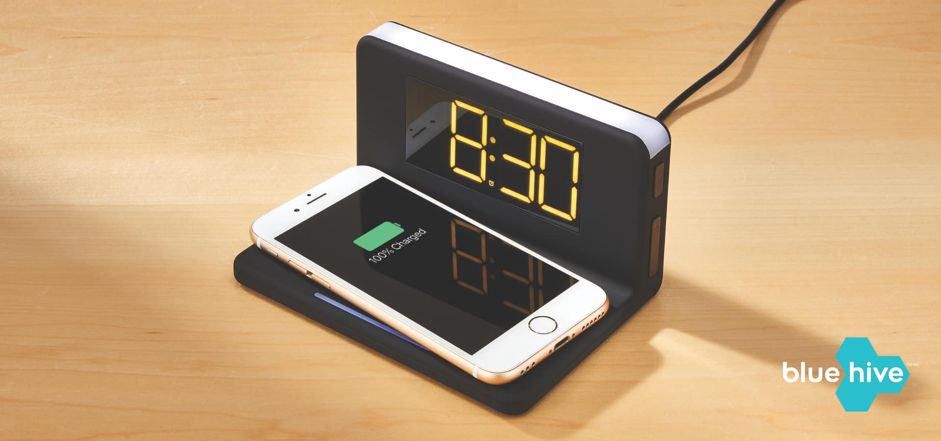 A black Bluehive Wireless Charger with Alarm Clock charging a white mobile phone.
