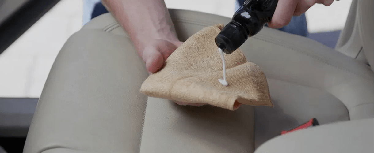 Person pouring liquid cleaner on a microfiber cloth in a vehicle interior.
