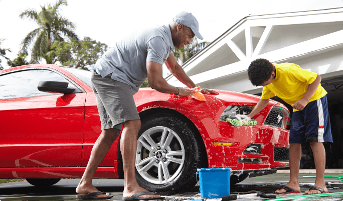 Man and boy wash a red mustang in a driveway.