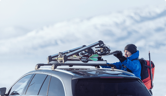 Un homme utilisant le porte-bagages de sa voiture pour fixer des planches neige.