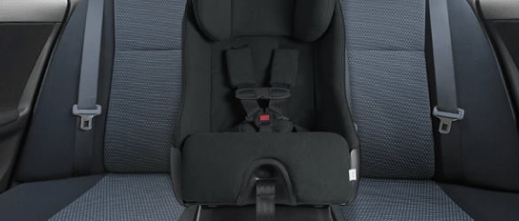 A black car seat affixed to the grey rear seat of a car.