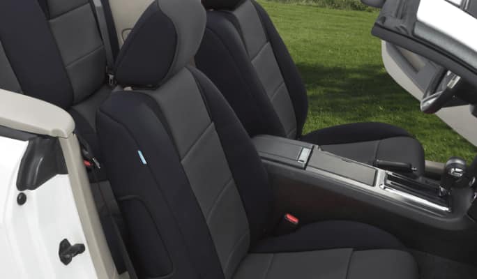 Black CoverKing seat covers protect the front and rear seats of a white convertible parked beside a lake.
