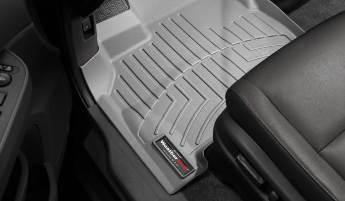 A light grey WeatherTech floor mat lines the driver’s-side footwell of a car with a black interior.