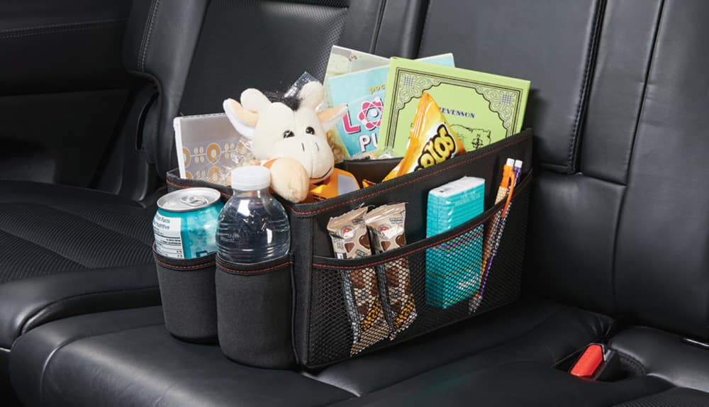 A car organizer on the back seat of a car, with various items in it. 