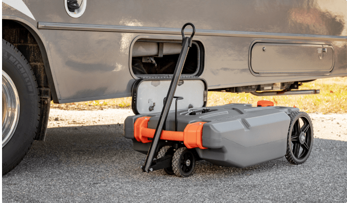 A 21-gallon grey-and-orange Camco Rhino Heavy-Duty Portable Waste Holding Tank rests on the ground connected to a grey RV.