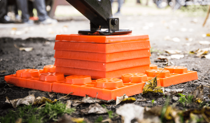 Close-up image of an RV stabilizer post mounted atop several orange levelling blocks.