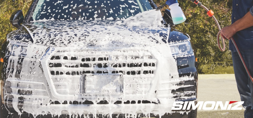 Man using a pressure washer to clean a car.