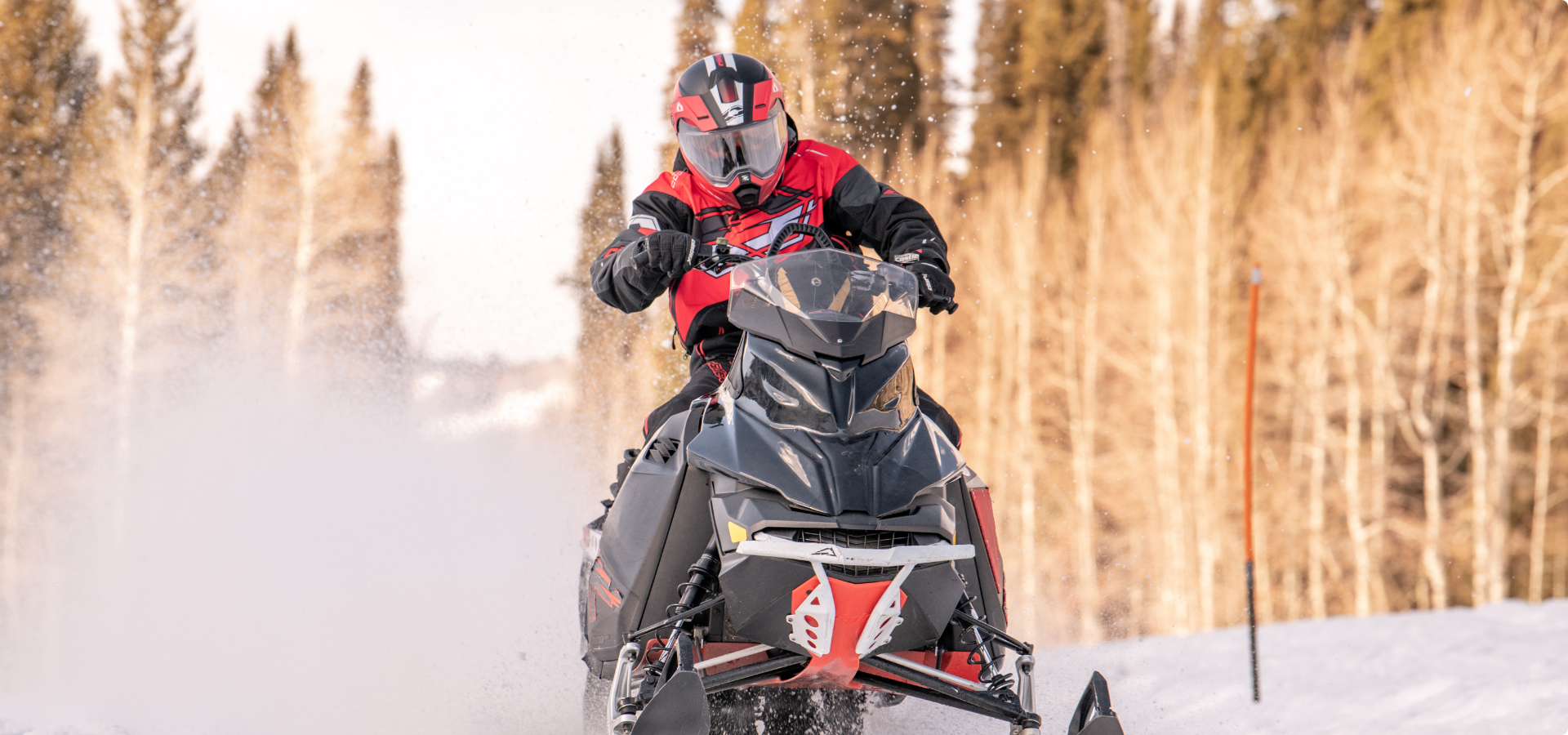 A helmeted man drives a red snowmobile through snow.