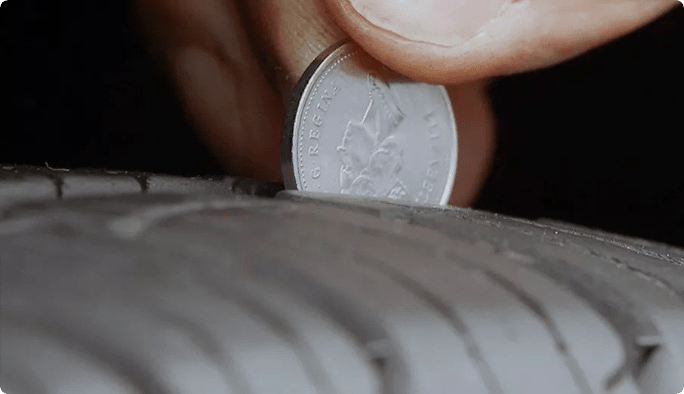 Une main qui place une pièce de monnaie canadienne de cinq cents dans la bande de roulement d’un pneu.