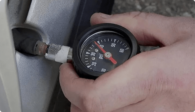 A hand applies a tire-pressure gauge to a tire’s valve stem. 