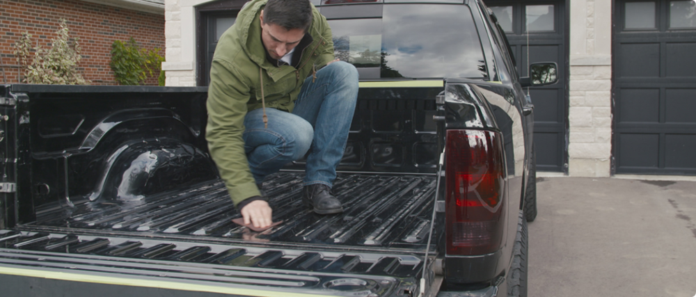 Man kneels in and inspects the bed of a black truck.