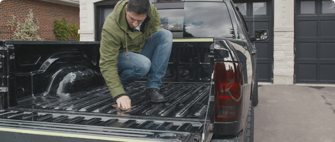 Un homme s'agenouille et inspecte le plateau d'un camion noir.