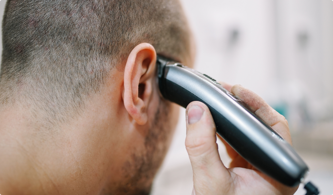 Man holds a hair trimmer above his right ear.