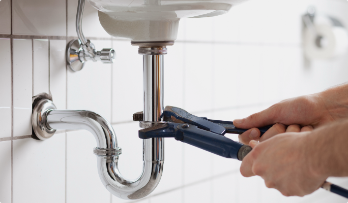 Une personne utilisant une clé à molette sur un tuyau de lavabo de salle de bain.