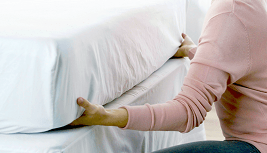 Person tucks the edges of a top sheet under a mattress.