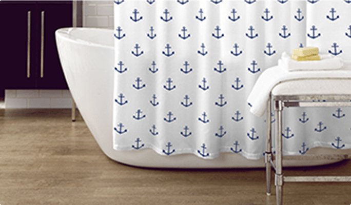 White shower curtain with blue anchor pattern over a white freestanding bathtub.