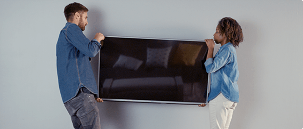 Man and woman holding a large flat screen TV before they mount it on a wall.