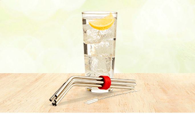 A set of stainless steel straws in front of a glass of ice water with an orange slice.