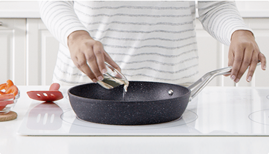A woman pouring oil into a non-stick frying pan.