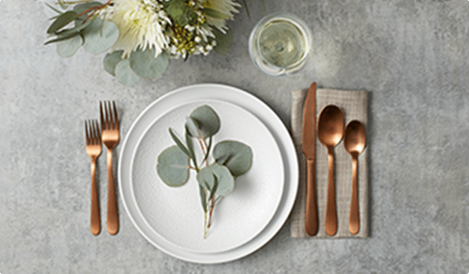 A place setting with white plates and copper-toned cutlery.