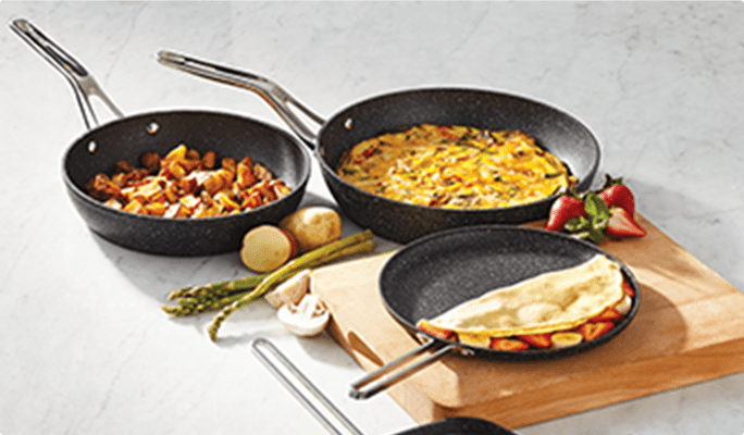 Three frying pans with crepes, breakfast hash, and scrambled eggs.