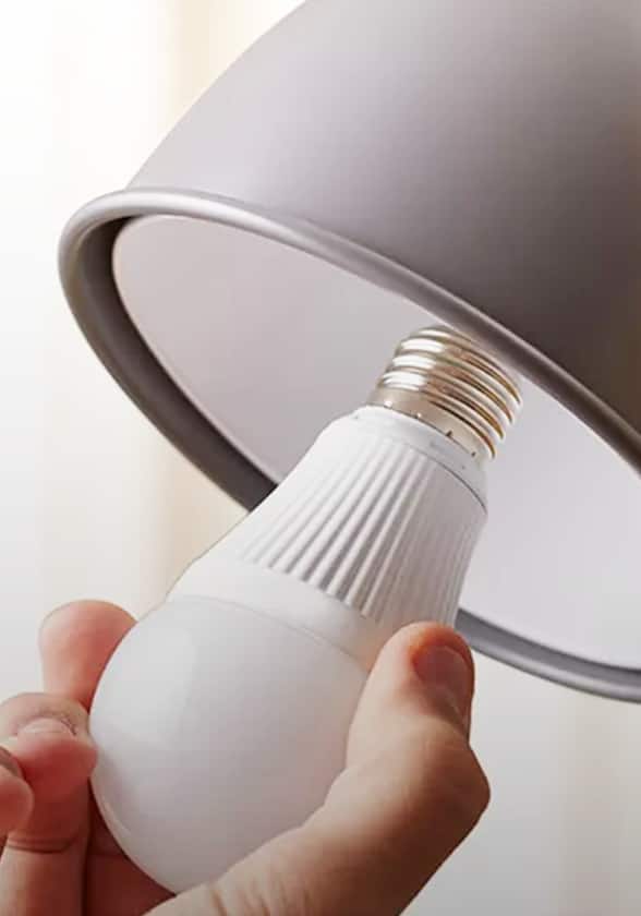 A hand screws a light bulb into a light fixture.