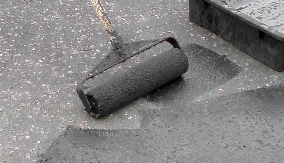 A roller spreads driveway sealer along asphalt.