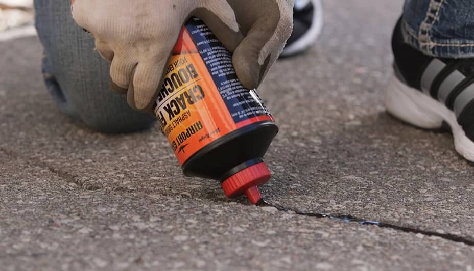 A hand applies driveway crack filler onto asphalt.