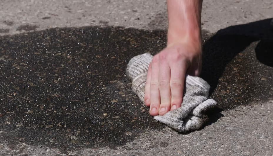 A hand wipes a stain on asphalt with a rag.